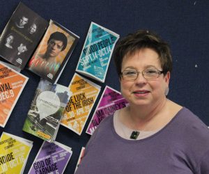Retiring English teacher stands in front of a bulletin board in her classroom.
