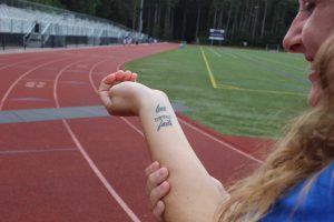 Kyra Arsenault shows off her tattoo, "Love never fails," at cross country practice on September 29 (Photo/ Delaney Murphy).
